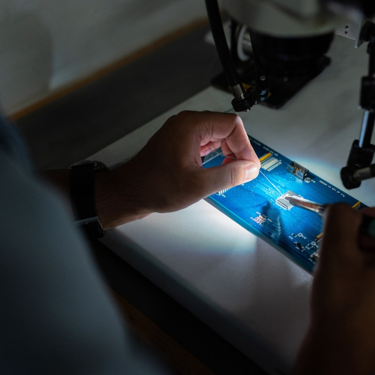 An engineer solders a blue circuit board
