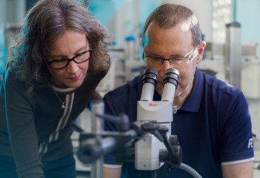 Two people working with microscope.