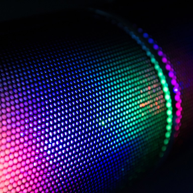 A bluetooth loudspeaker reflecting the purple, green and blue colours.