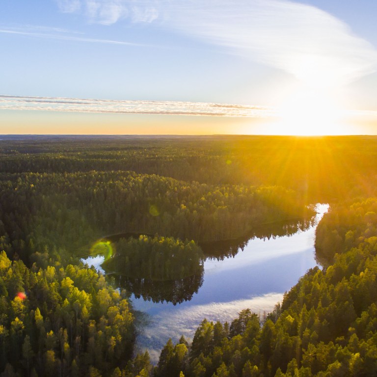 Aerial image of Nuuksio National Park in Espoo, Finland with the sun rising in a landscape of forests and lakes.