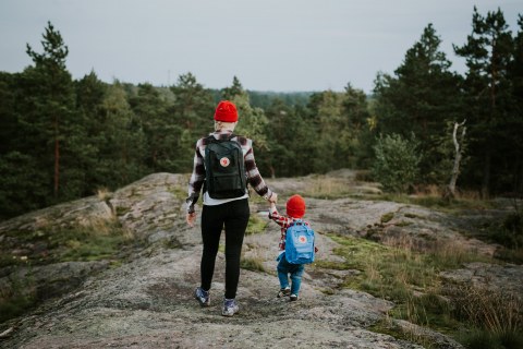 A woman and a boy are walking in forest and holding hands.