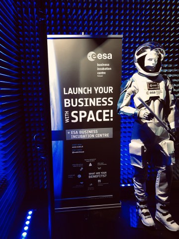 A life-size astronaut figure standing next to a roll up in a dark blue lit room.