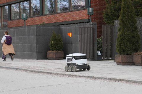 Food delivery robot drives past a woman carrying a bagpack