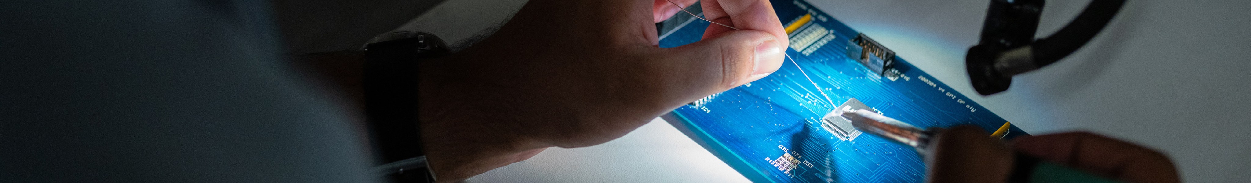 An engineer solders a blue circuit board