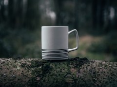 A steaming ceramic coffee cup on a tree trunk in a forest.